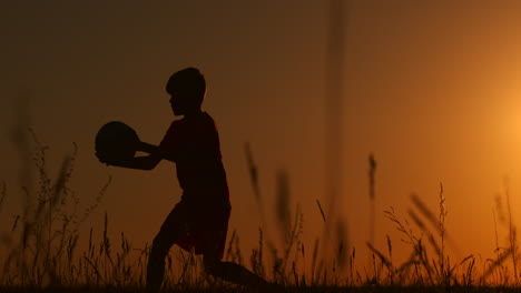 A-young-young-boy-football-player-trains-playing-with-a-ball-stuffing-on-his-leg-at-sunset-in-slow-motion-during-the-Golden-hour-in-the-field-until-sunset.-Training-from-dusk-to-dawn.-Concept-path-to-success